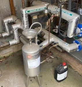 Chemical dosing pot installed in a plant room used to safely introduce water treatment chemicals into a heating hot water system.